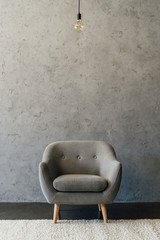 Cozy modern grey armchair and light bulb hanging in empty room