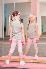 Girl child doing fitness exercises with dumbbells in health club, stretching in exercise, workout