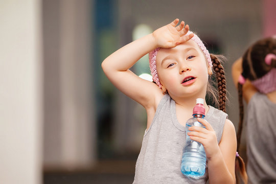 Girl child is tired after training fitness exercises in health club, drink water.