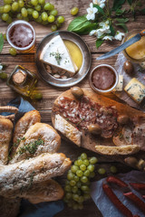Homemade baguette, cheese, olives, grapes, flowers on old boards