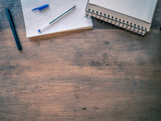 Top view of spiral notebook, maths notebook and pens on wooden table. Room for copy.