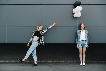 Attractive young girlfriends posing with bunch of balloons outdoors