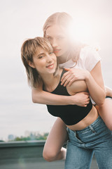 Beautiful young lesbian couple piggybacking and smiling at camera