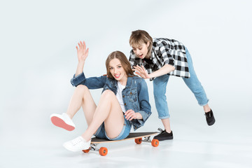 Attractive happy young girlfriends having fun with skateboard isolated on grey