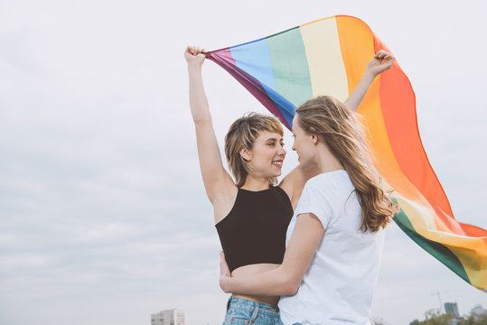 Smiling young homosexual couple holding lgbt flag and hugging outdoors