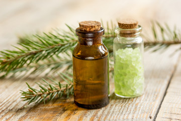 cosmetic spruce oil and salt in bottles with fur branches on wooden table background