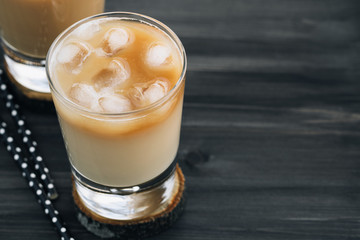 Close-up of a refreshing iced coffee with milk in glasses on a wooden black table.