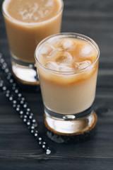 Close-up of a refreshing iced coffee with milk in glasses on a wooden black table.
