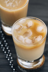 Close-up of a refreshing iced coffee with milk in glasses on a wooden black table.