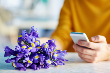 Closeup portrait of unrecognizable young man using smartphone while waiting for date with bouquet of flowers