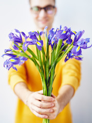 Portrait of smiling young man presenting bouquet of flowers to camera, focus on beautiful irises