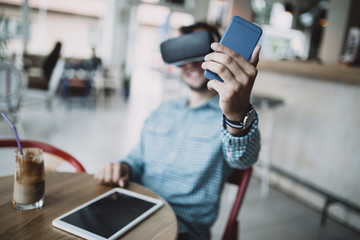 Young handsome man sitting in cyber cafe and using virtual reality headset or glasses.