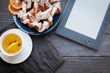 E-book and Bavarian cream puff with crushed hazelnut and lemon fudge on a blue plate. In the background a cup of green tea with lemon and cinnamon sticks. Top view with copy space