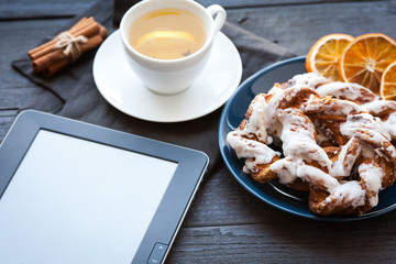 E-book and Bavarian cream puff with crushed hazelnut and lemon fudge on a blue plate. In the background a cup of green tea with lemon and cinnamon sticks