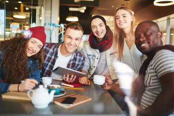 Cheerful coworkers distracted from project discussion and posing for photography with wide smiles in lovely cafe, waist-up group portrait