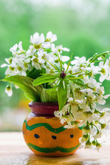 A bouquet of flowers birdcherry tree and grass forest in orange wooden pot, close-up
