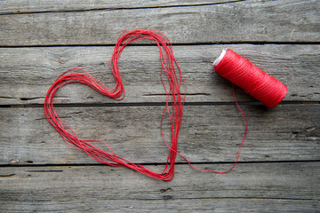 Heart sign made from red thread on wooden surface