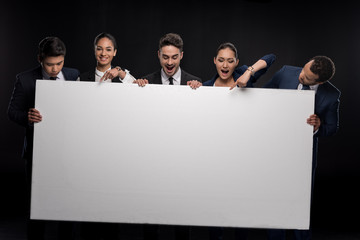 Group of excited business people pointing on blank billboard isolated on black