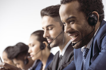 Fototapeta premium Close-up view of smiling call center operator in headset working with colleagues behind