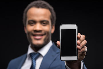 Portrait of businessman presenting smartphone with black screen isolated on black