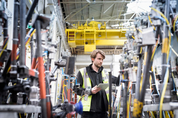 Engineer inspecting press machinery in car factory