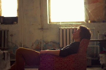 Young man sitting on vintage armchair in artist studio gazing upward