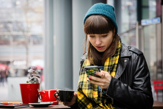 Young woman at sidewalk cafe looking at smartphone