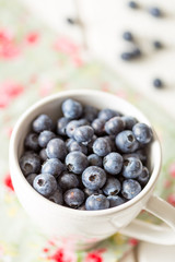Close Up View of Fresh Blueberries in a White Cup on White Wooden Table, Vertical View
