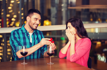 man giving engagement ring to woman at restaurant