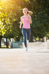 Pretty sporty woman jogging at park in sunrise light