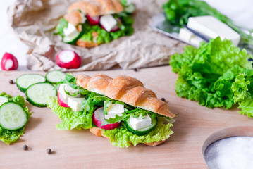Croissant sandwich with cheese and vegetables for healthy snack, craft paper and greens background. Picnic summer food. Selective soft focus