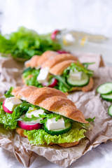 Croissant sandwich with cheese and vegetables for healthy snack, craft paper and greens background. Picnic summer food. Selective soft focus