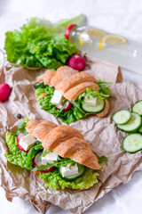 Croissant sandwich with cheese and vegetables for healthy snack, craft paper and greens background. Picnic summer food. Selective soft focus