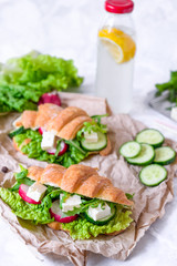 Croissant sandwich with cheese and vegetables for healthy snack, craft paper and greens background. Picnic summer food. Selective soft focus