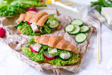 Croissant sandwich with cheese and vegetables for healthy snack, craft paper and greens background. Picnic summer food. Selective soft focus