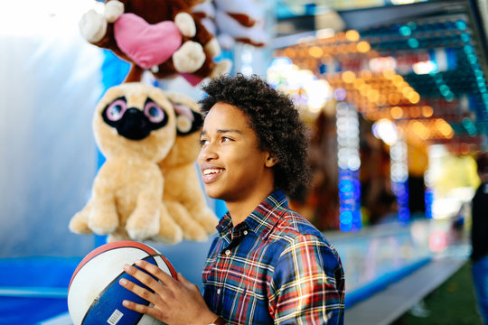 Young boy at funfair, playing on fairground stall, holding basketball