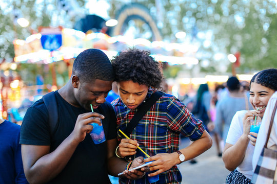 Group of friends at funfair, two boys looking at smartphone