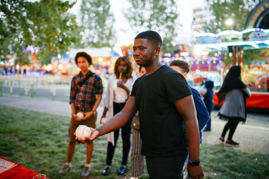 Group of friends at funfair, boy holding ball, looking towards fairground stall