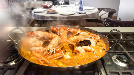 Pot of boiling paella on the stove with a dinner table on the back