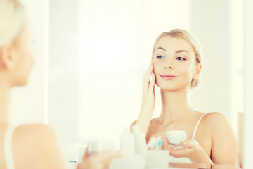 happy woman applying cream to face at bathroom