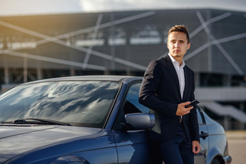 Attractive handsome businessman with  smartphone near the car