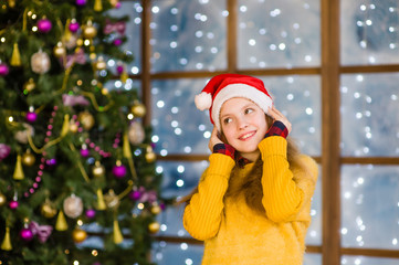 Portrait of blonde teen girl in red santa hat on the background of Christmas tree