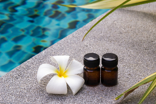Bottles of aroma essential oil and flower of frangipani (or plumeria) on the swimming pool background for spa theme.
