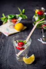 Flavored water with fresh strawberries and mint in glass on a black wooden table with bright details.Selective focus, close up