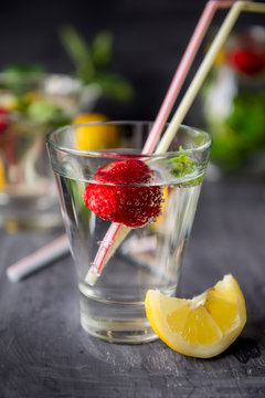 Flavored water with fresh strawberries and mint in glass on a black wooden table with bright details.Selective focus, close up