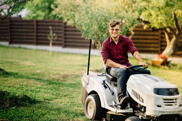 Smiling man riding a lawnmower and doing landscaping works