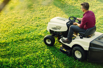 Gardening works with young male cutting grass. Industrial lawn mower in action