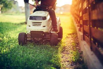 Close up details of landscaping and gardening. Worker riding industrial lawnmower