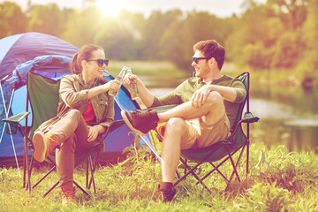 happy couple clinking drinks at campsite tent