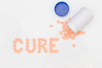 Orange pills spill put of the bottle and arranged in the word Cure.